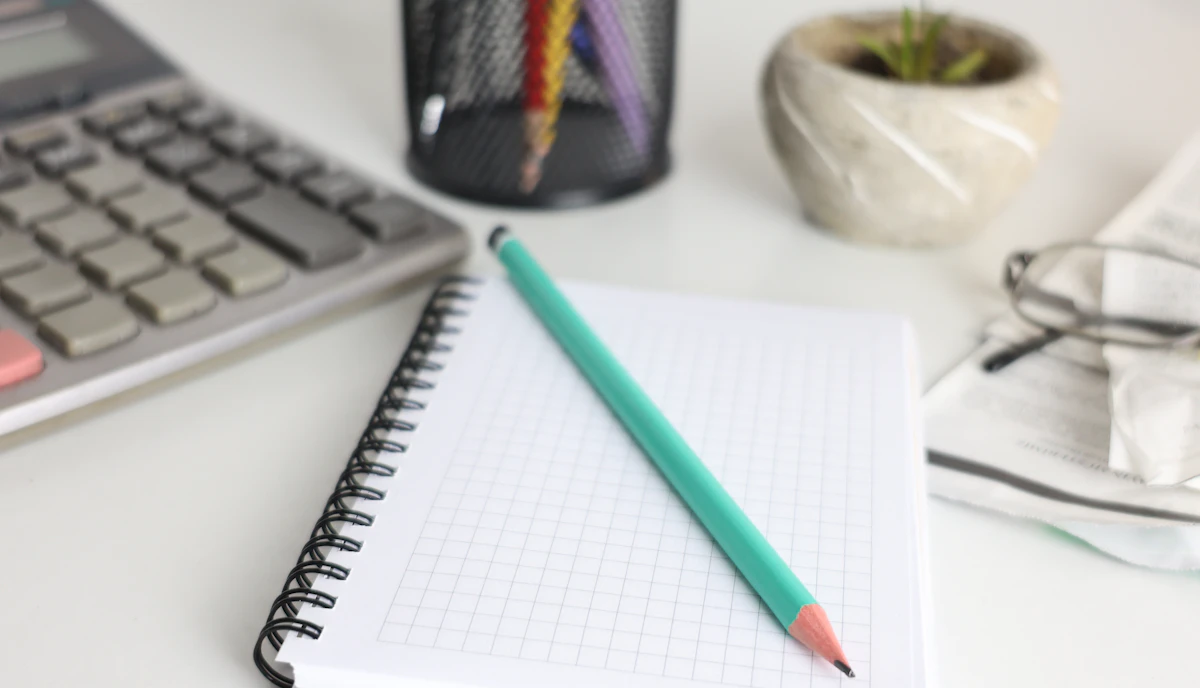 A desk with a calculator, notebook, pencil and plant